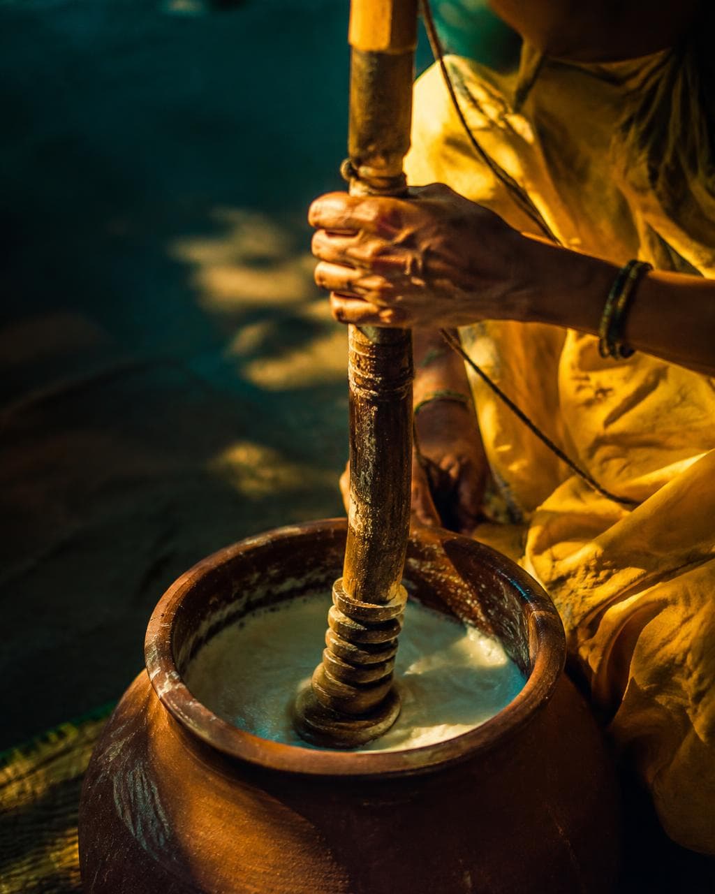 Artisan hand-churning curd using traditional two-way wooden bilona in earthen clay pot